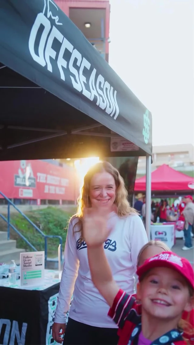 A smiling child waving beside an athlete in a Bulldogs shirt beneath the Offseason canopy